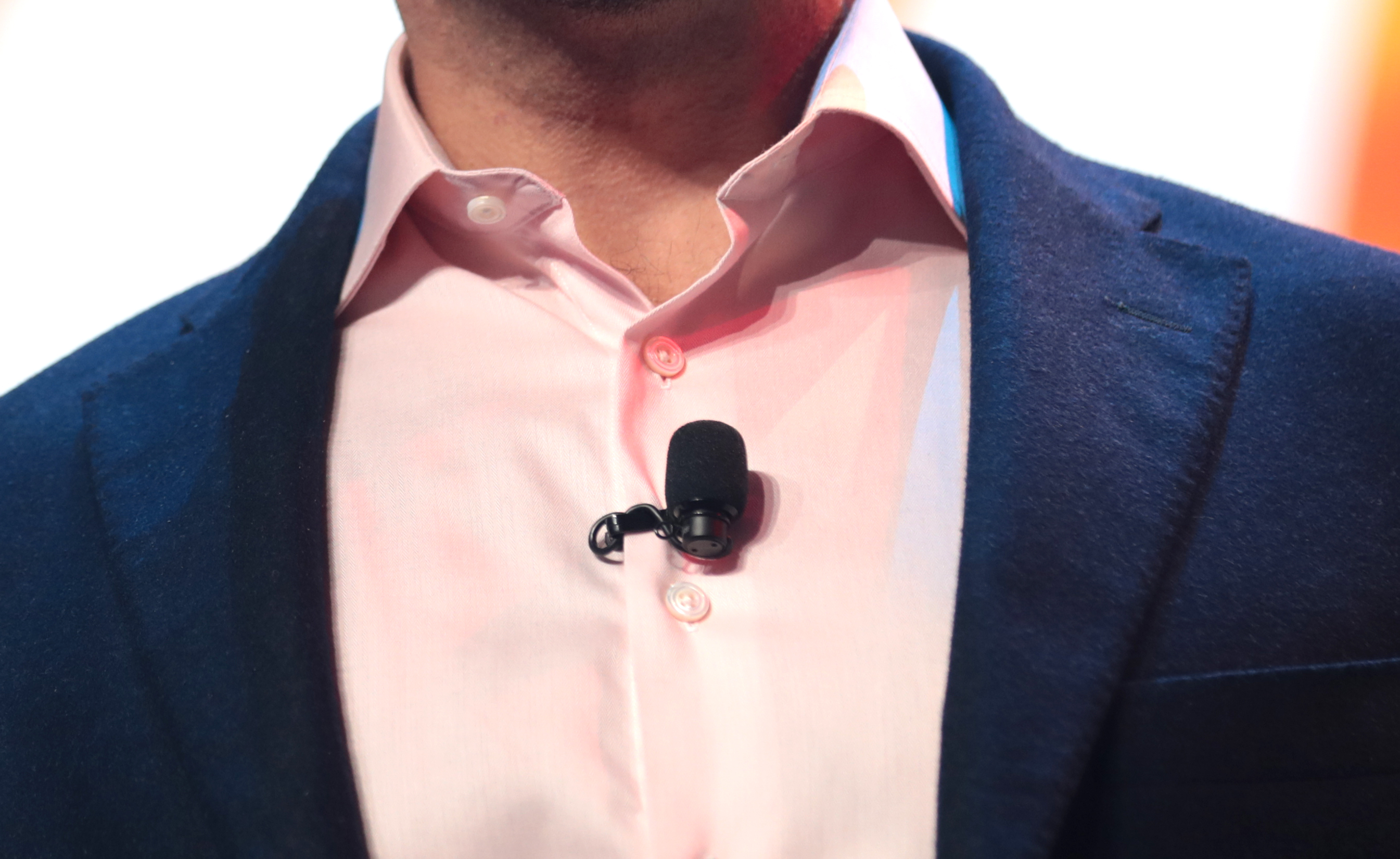 Black lavalier microphone with a foam windscreen clipped to a pink shirt between jacket lapels.