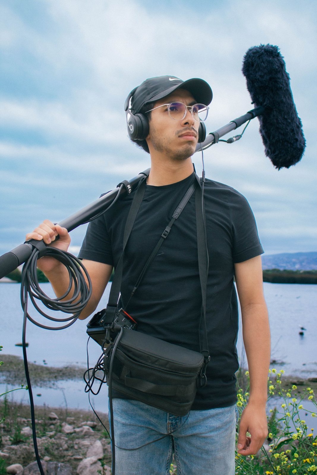 A sound recordist outdoors with a boom pole and headphones.